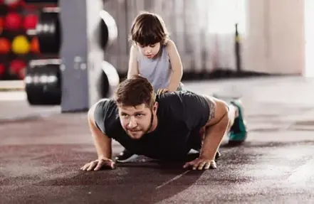 An athlete does a pushup with his child sitting on his back.