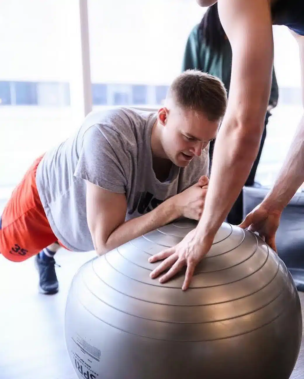 An athlete does core exercises on a medicine ball with guidance from his coach