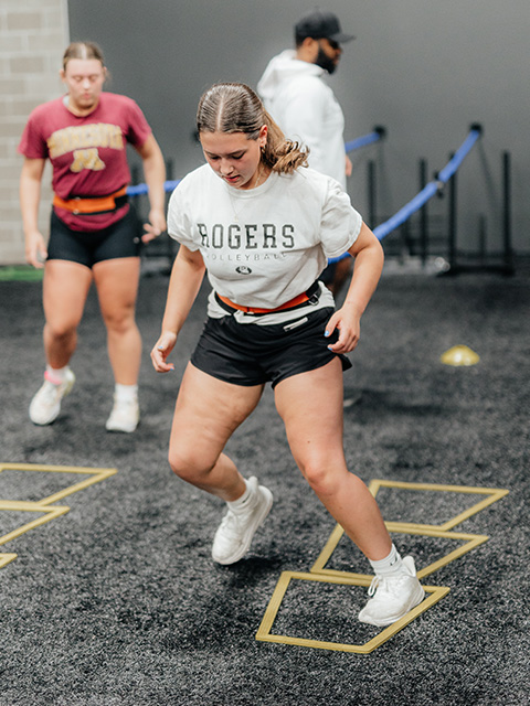 A pair of athletes perform footwork drills while guided by a sports performance coach.