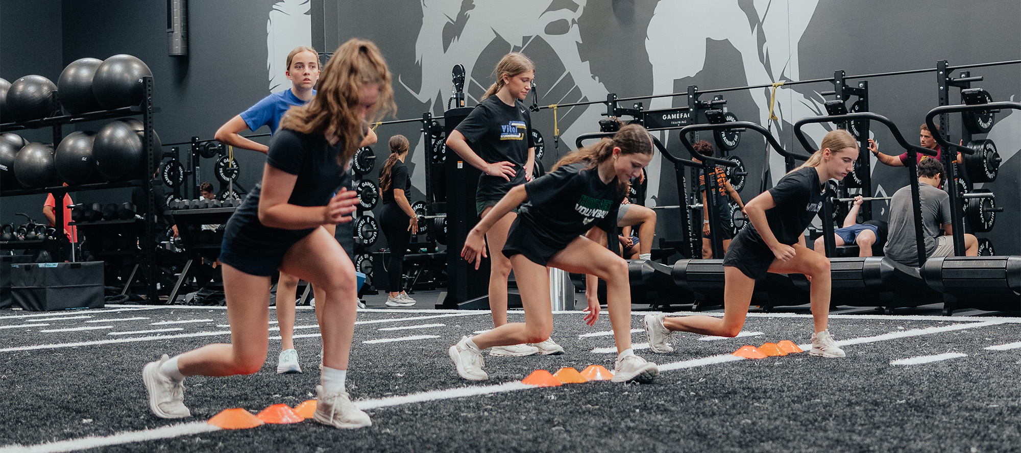 A pair of athletes perform footwork drills while guided by a sports performance coach.