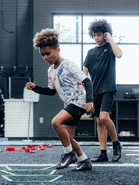 Two children work on agility drills on the TRIA GameFace turf.