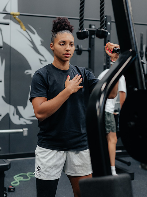 An athlete strengthens her shoulder using a weight machine in the TRIA GameFace strength training area.