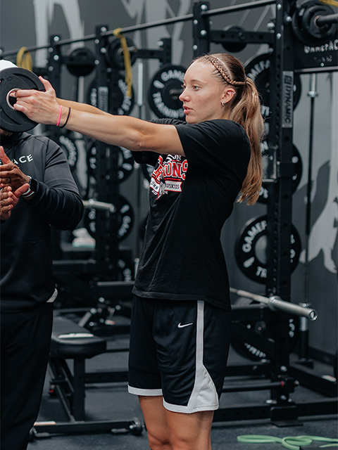 An athlete strengthens her shoulder using a weight machine in the TRIA GameFace strength training area.