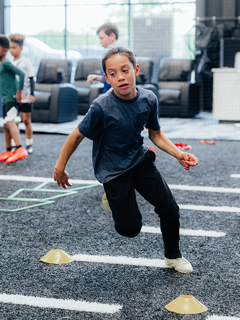 A child athlete runs between cones on the indoor turf.
