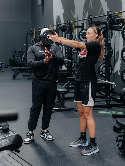 A trainer helping an athlete with a drill using a weight plate.
