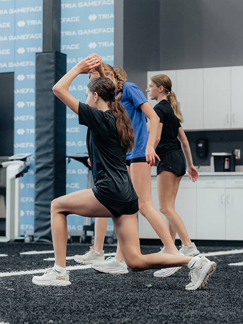 A team of young athletes do lunges across the indoor turf.